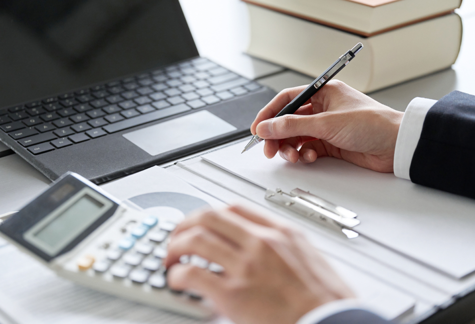 ノートパソコン、電卓、書類を使って業務を行う様子