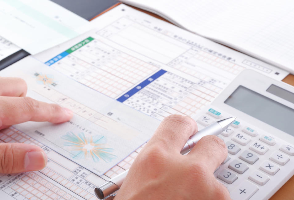 書類と電卓を使って作業を行う手のクローズアップ